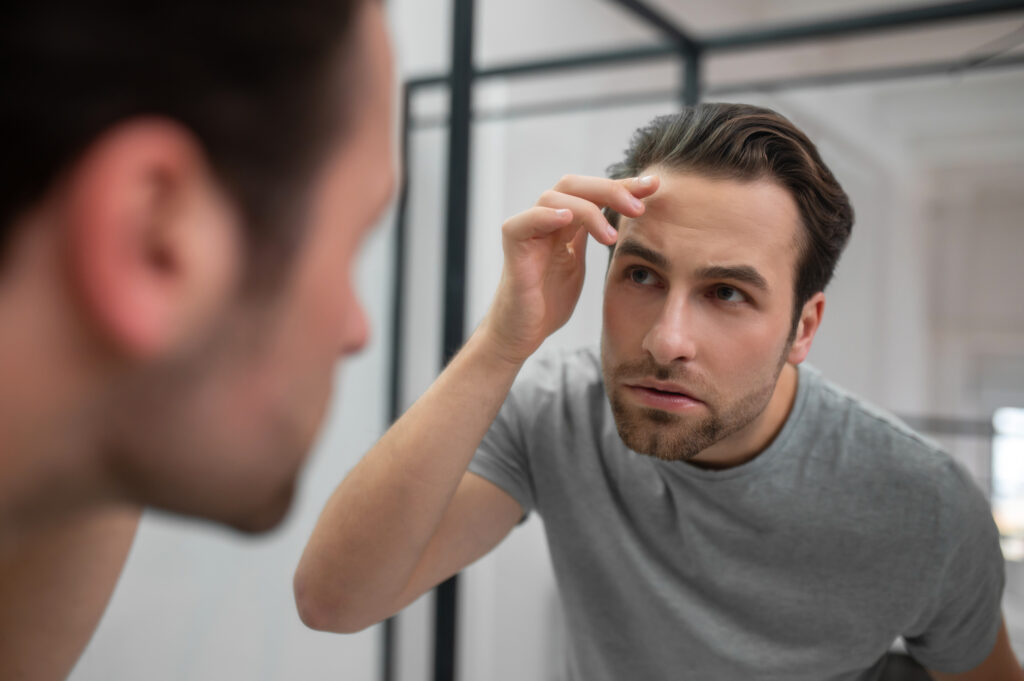 A young man in grey tshirt looking at his reflection in the mirror